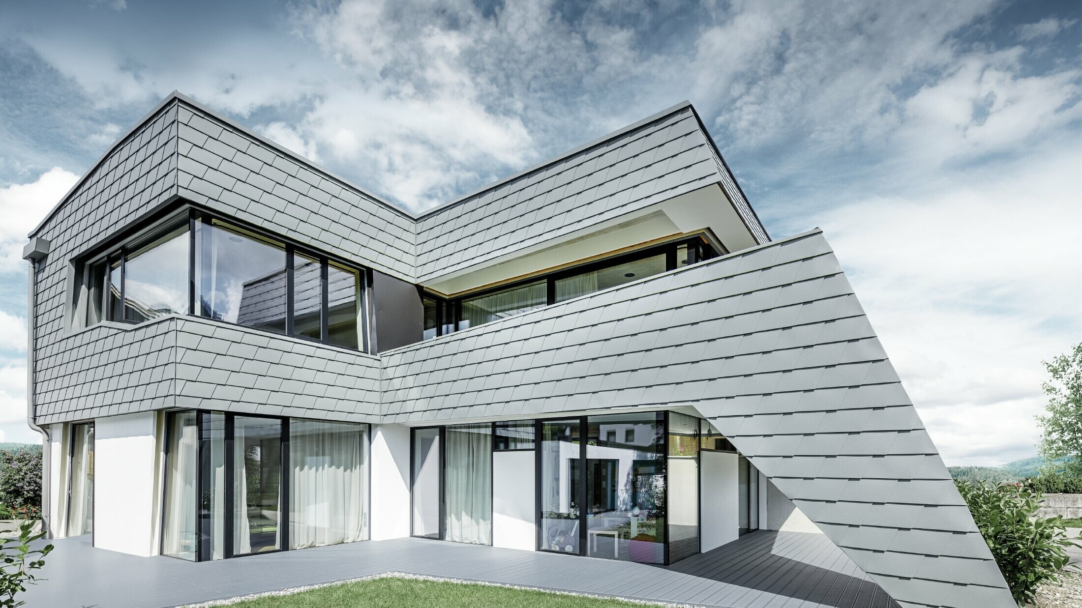 Modern lapostetős családi ház nagy üvegfrontokkal és világosszürke PREFA alumínium zsindely homlokzatburkolattal