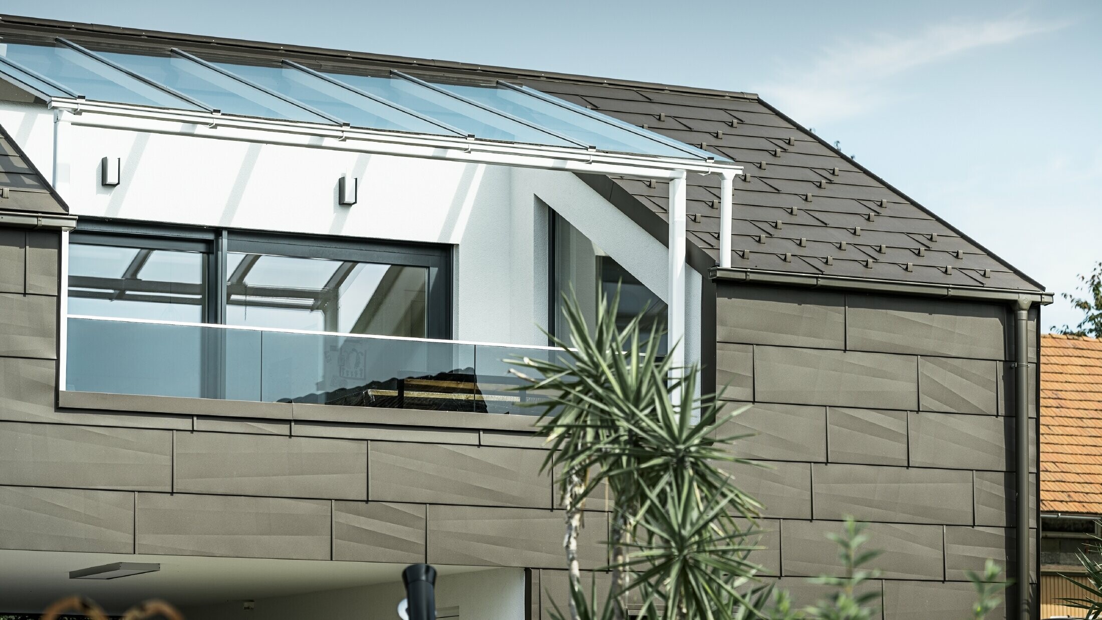 Bővítés PREFA komplett rendszerrel burkolt tetőterasszal, FX.12 PREFA tető- és homlokzatpanellel a tetőn és a homlokzaton. Ezenkívül a PREFA négyszögszelvényű ereszcsatorna PREFA lefolyócsővel és barna színű, gazdag tartozékokkal a tető-vízelvezetéshez.