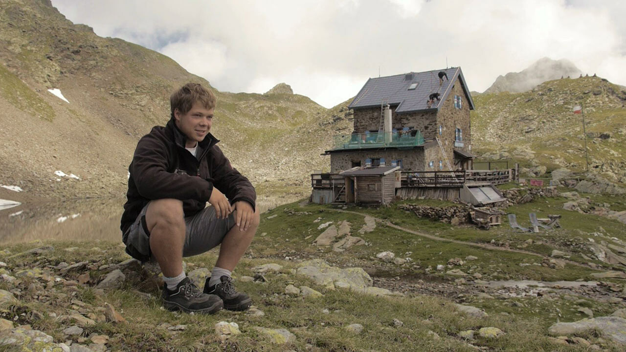 Jakob Schöttl szakmunkástanuló egy sziklán ül. A háttérben a „Flagger Schartenhütte” látható, melyet újonnan PREFA tetőpanellel fedtek be.