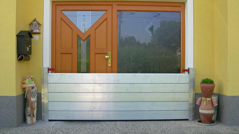 Családi ház bejárati ajtaja a modern PREFA árvízvédelmi rendszerrel