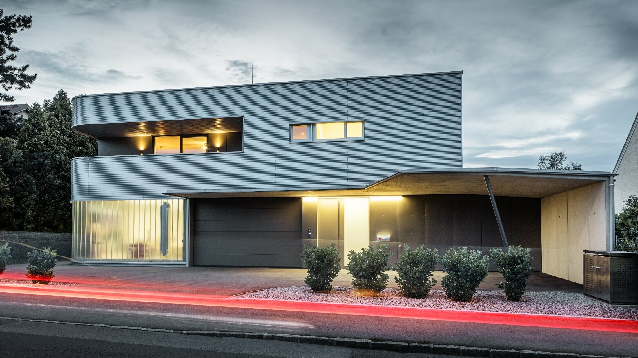 Modern lakóház natúr alumínium homlokzattal a PREFA profilhullámból garázzsal, esti fényben fényképezve
