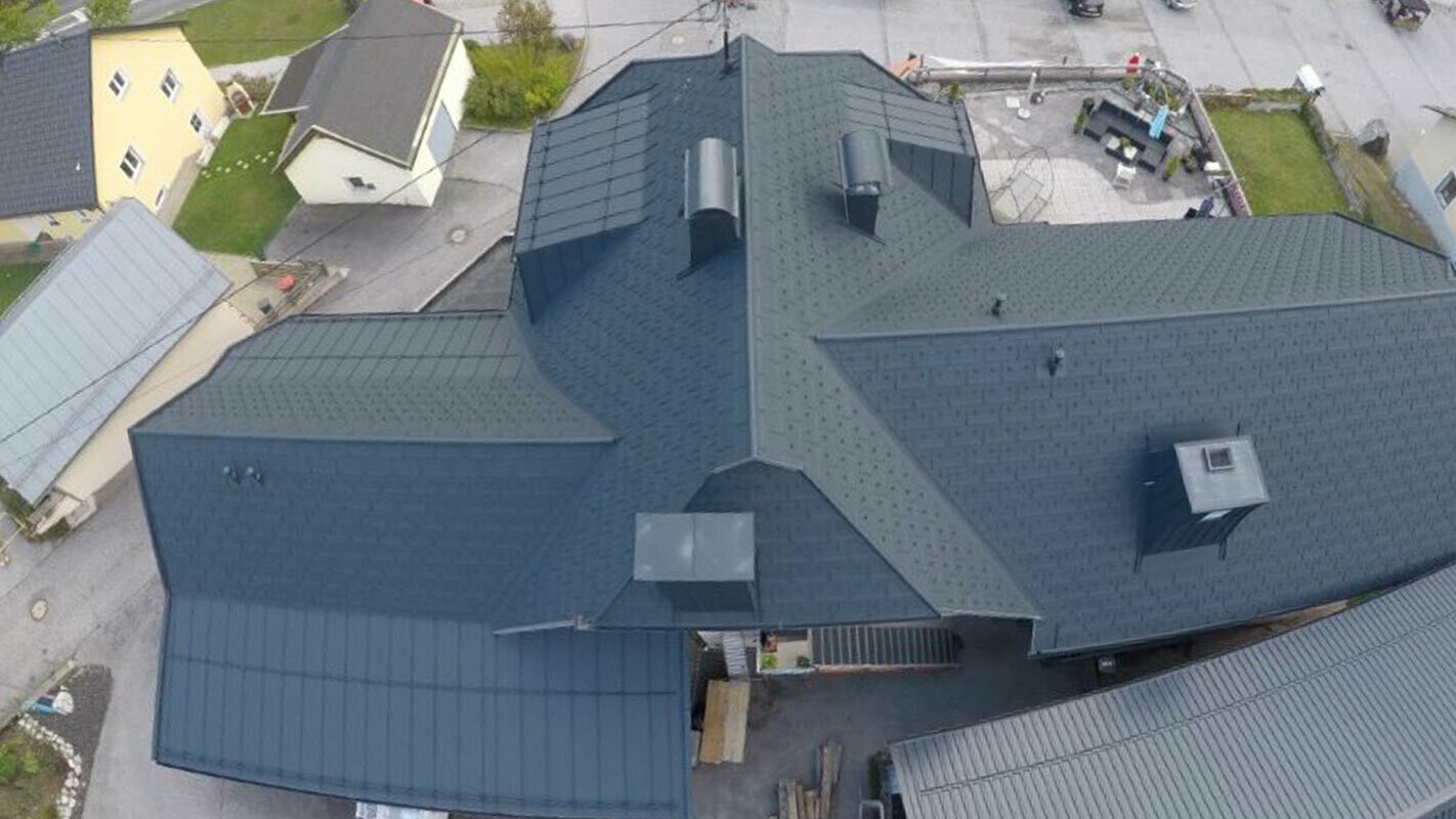 Nagy tetőfelület felújítása, részletekkel – vápák, tetőablakok és kémény. A tetőt antracit színű, PREFA R.16-os alumínium Classic elem fedi.