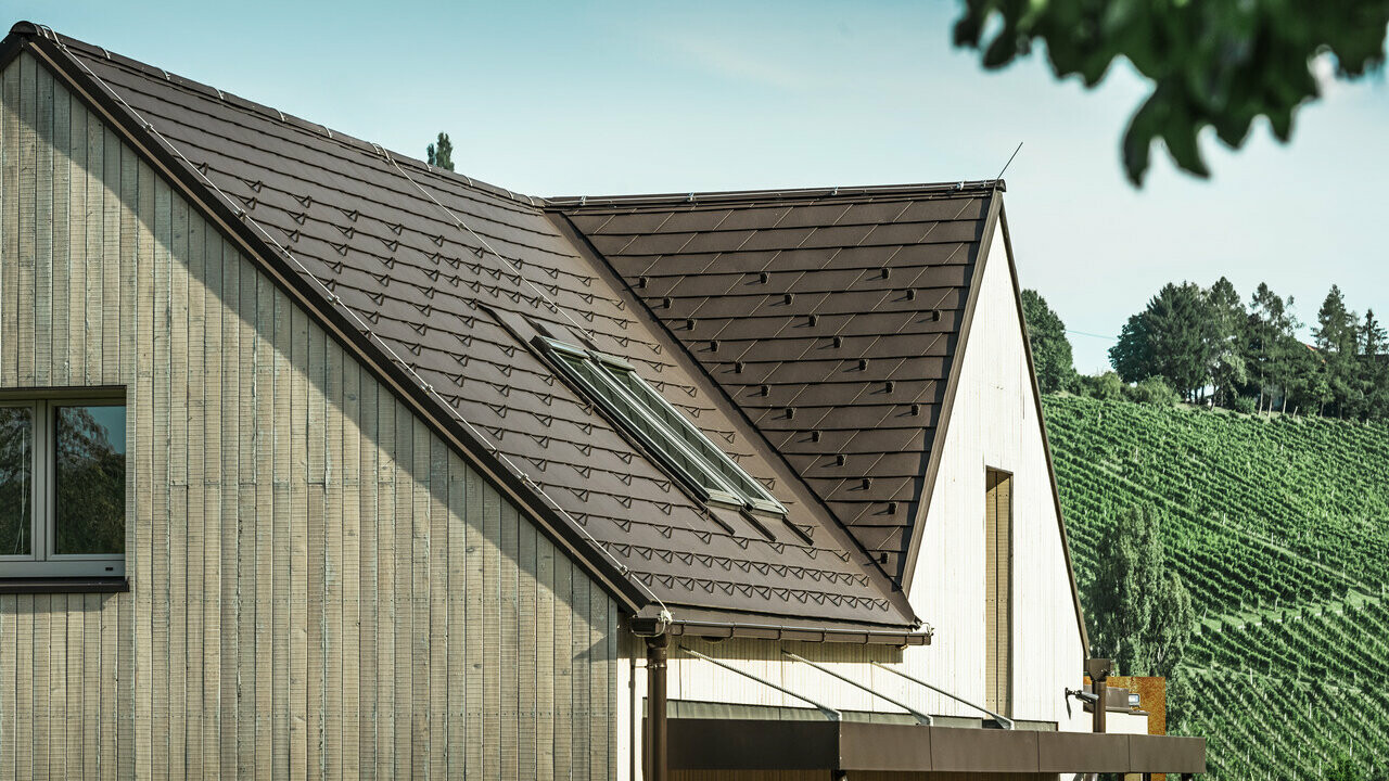 A két nyeregtetős családi házat dióbarna PREFA tetőfedő zsindely borítja. A tető-vízelvezetése a PREFA négyszögszelvényű ereszcsatornán keresztül történik. A homlokzat egy részét viharvert fa borítja.