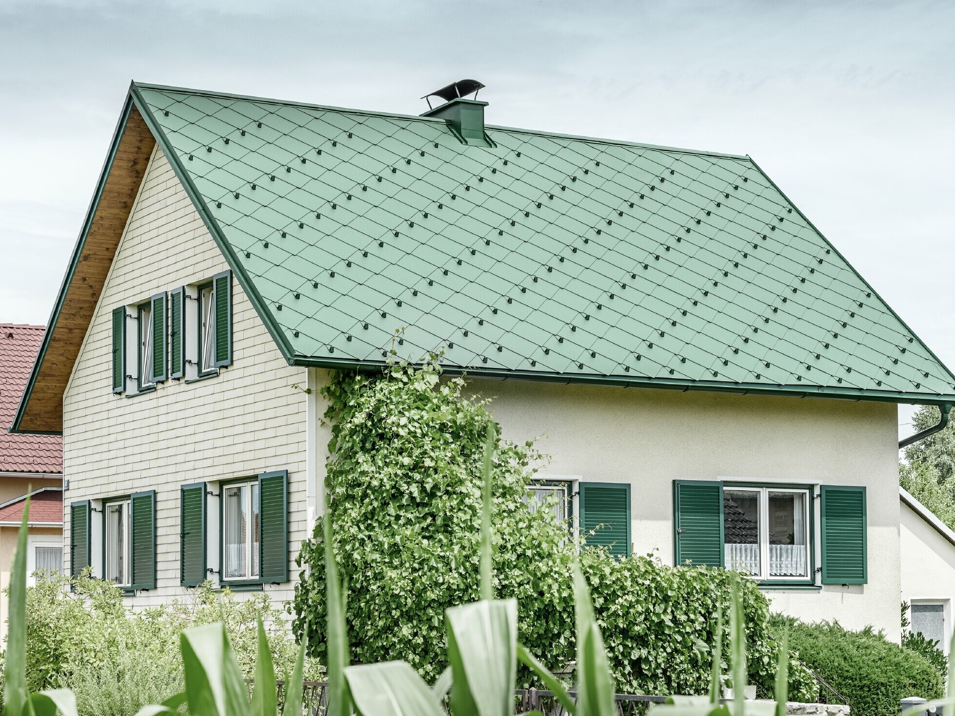 Klasszikus családi ház nyeregtetővel,mohazöld alumínium tetőfedéssel,zöld redőnyökkel
