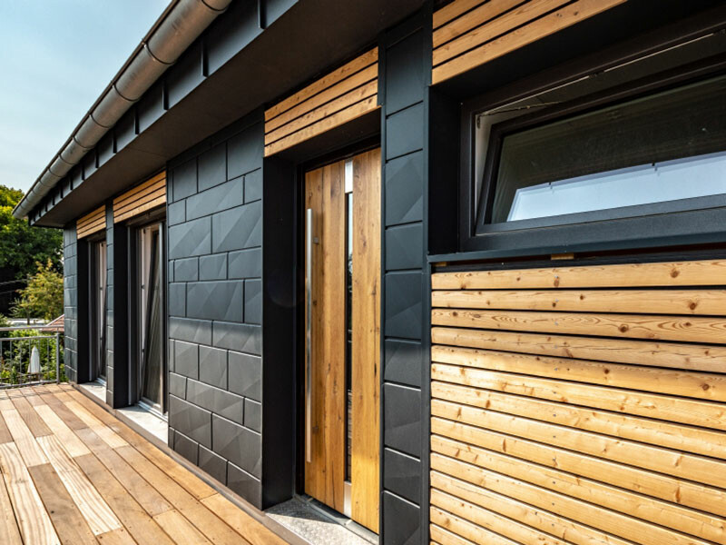 Modern családi ház szép antracit színű PREFA Siding.X homlokzatpanelekkel és fa elemekkel.