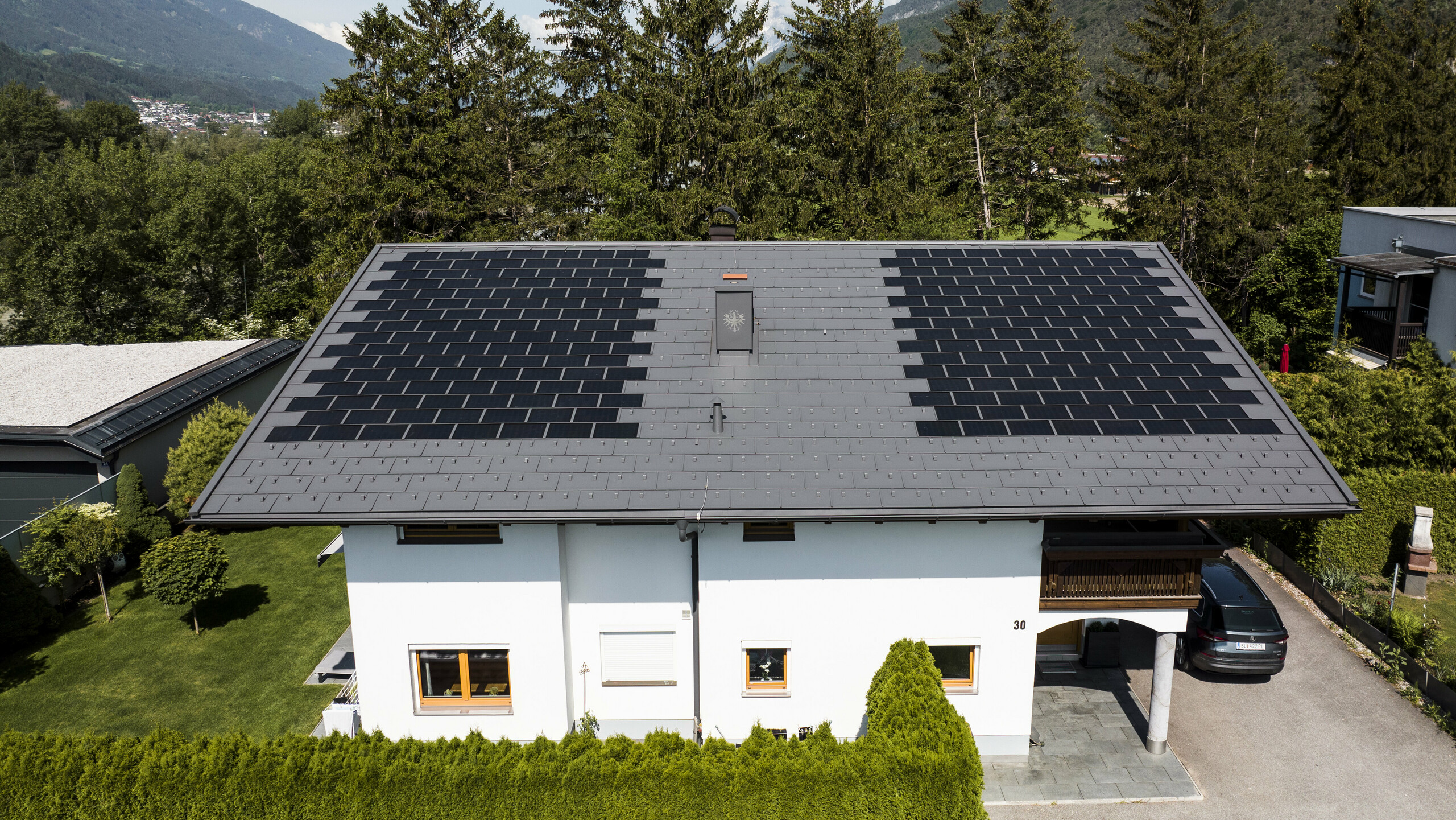 Zu sehen ist ein Einfamilienhaus eingedeckt mit der PREFA Solardachplatte klein mit Dachplatte R.16 in der Farbe P.10 Dunkelgrau in ländlicher Umgebung.