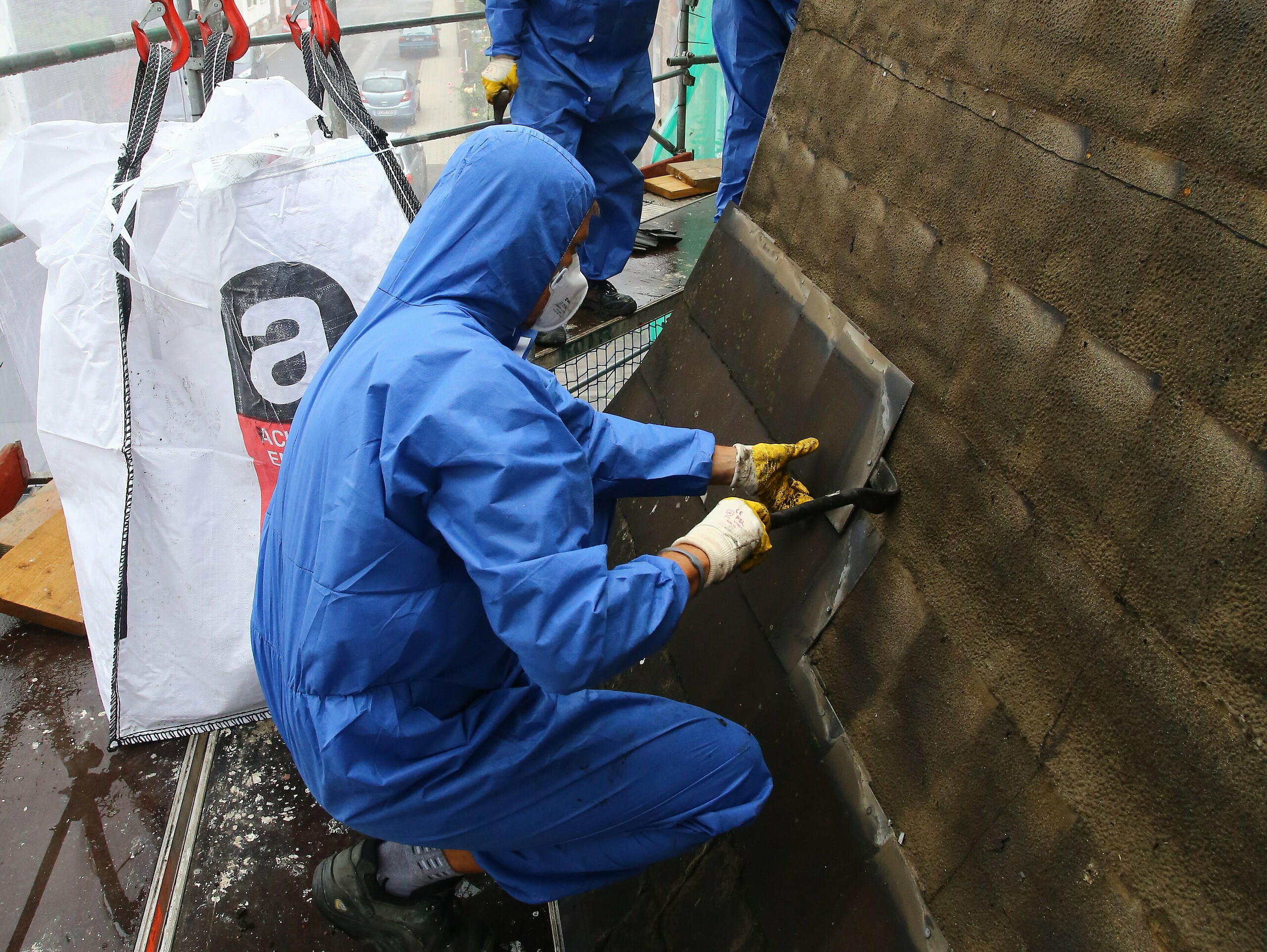 Képzett munkás az azbeszttartalmú, régi tetőfedés eltávolításakor védőmaszkot használ, amely megakadályozza az azbeszt belégzését