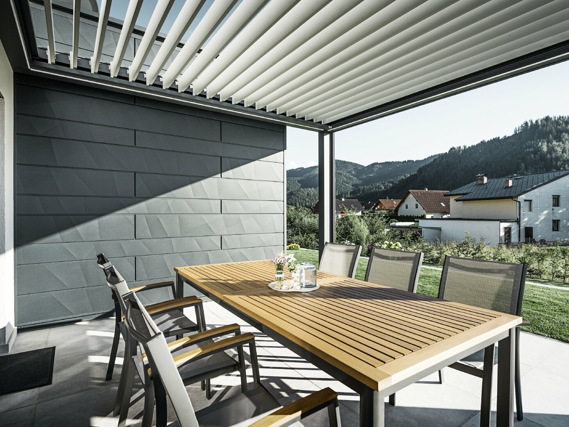 Lamellákkal fedett, védett terasz asztallal és székekkel; a homlokzat egyik oldala PREFA Siding.X antracit homlokzatburkoló panelekkel van burkolva.