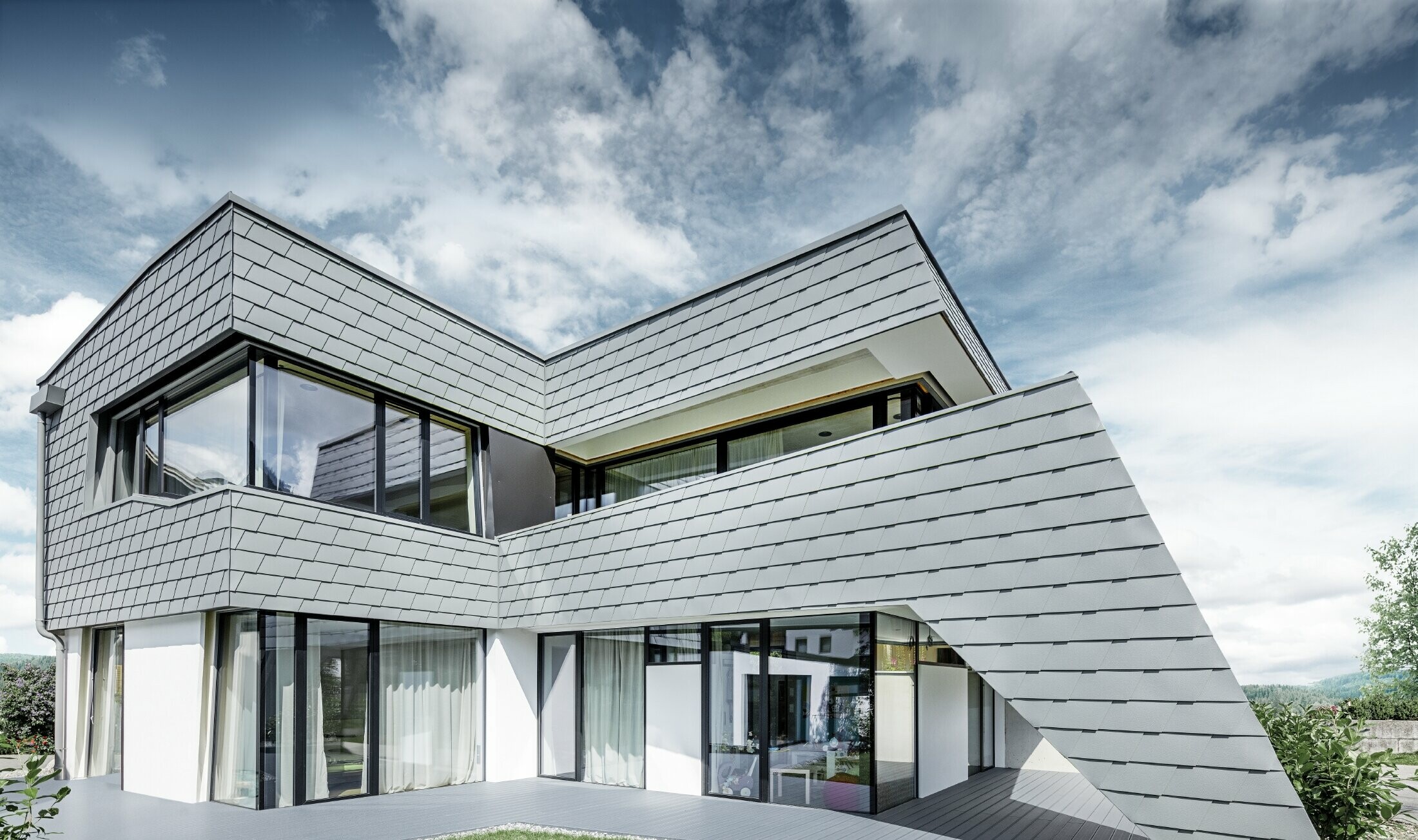 Modern lapostetős családi ház nagy üvegfrontokkal és világosszürke PREFA alumínium zsindely homlokzatburkolattal