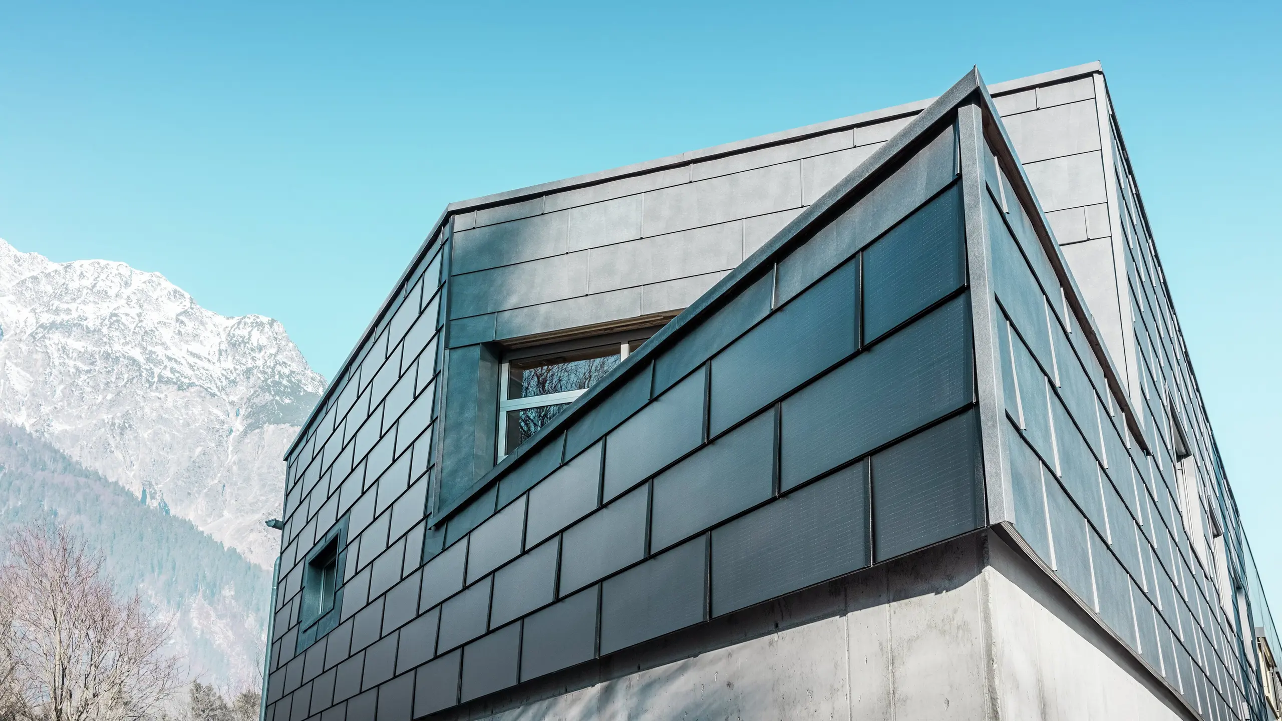 Modern homlokzat a PREFA napelemes tetőlemezekkel: a fenntartható alumíniumlemezek beépített fotovoltaikus rendszerrel áramot termelnek, és harmonikusan illeszkednek az építészeti kialakításba.