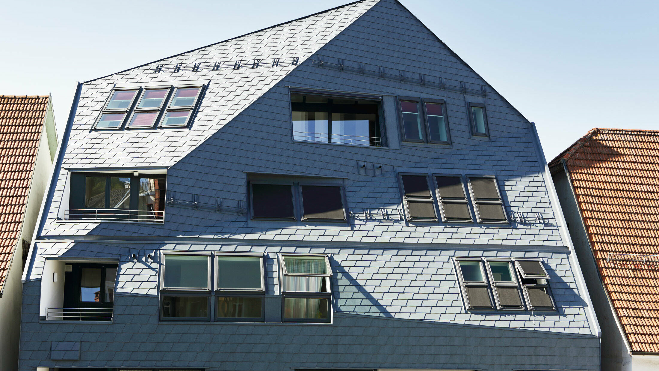 Galériaház szegélyezett homlokzattal, PREFA tetőfedő- és homlokzatburkoló zsindellyel, P.10 márványszürke színben, sok ablakkal