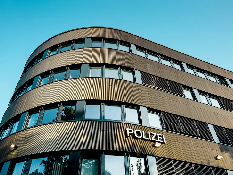 Dramatische Untersicht des geschwungenen Neubaus vom Polizeikommissariat 43 in Hamburg: Die markante PREFA Aluminiumfassade aus eloxierten Strangpressprofilen „Zacke“ in Mittelbronze zieht als architektonischer Eyecatcher alle Blicke auf sich. Die feine, rhythmische Struktur erzeugt dynamische Licht- und Schattenverläufe und betont die fließenden Rundungen des Baukörpers. PREFA Aluminium überzeugt durch hohe Witterungsbeständigkeit, Korrosionsschutz und Langlebigkeit – eine nachhaltige, wartungsarme Lösung für präzise, moderne Fassadenarchitektur.