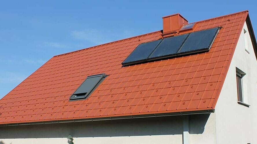 Családi ház téglavörös PREFA tetőlemezzel fedett nyeregtetővel. Tetőfelület napkollektoros rendszerrel és tetőablakkal