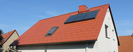 Családi ház téglavörös PREFA tetőlemezzel fedett nyeregtetővel. Tetőfelület napkollektoros rendszerrel és tetőablakkal
