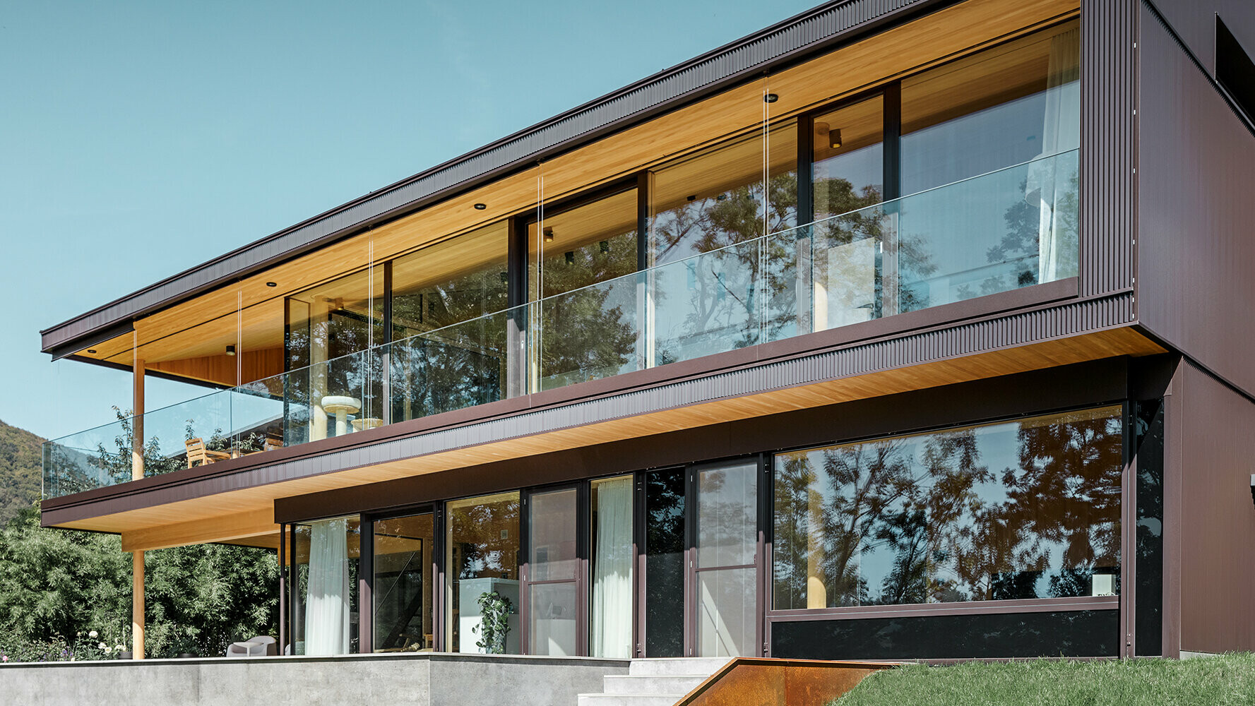 Új családi ház nagy üvegfelületekkel és barna színű alumíniumhomlokzattal