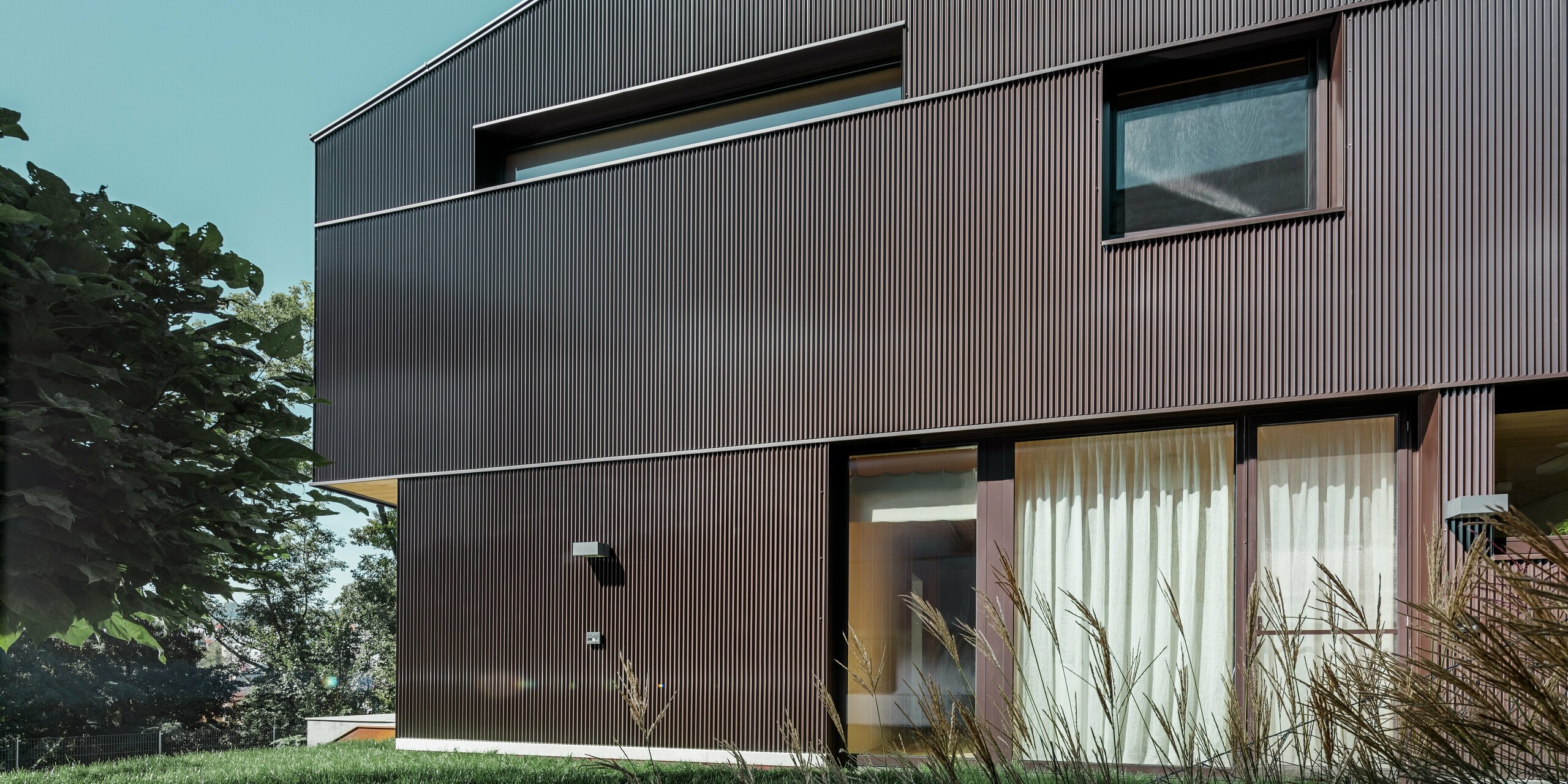 Dieses moderne Einfamilienhaus in Linz verfügt über eine Fassadenbekleidung aus stranggepresstem Aluminium. Das PREFA Zackenprofil in der Farbe Nussbraun verleiht dem Gebäude einen einzigartigen Look und bietet zudem zuverlässigen Schutz. Die spezielle Anordnung der Fenster betont die detaillierte Gestaltung des Gebäudes.