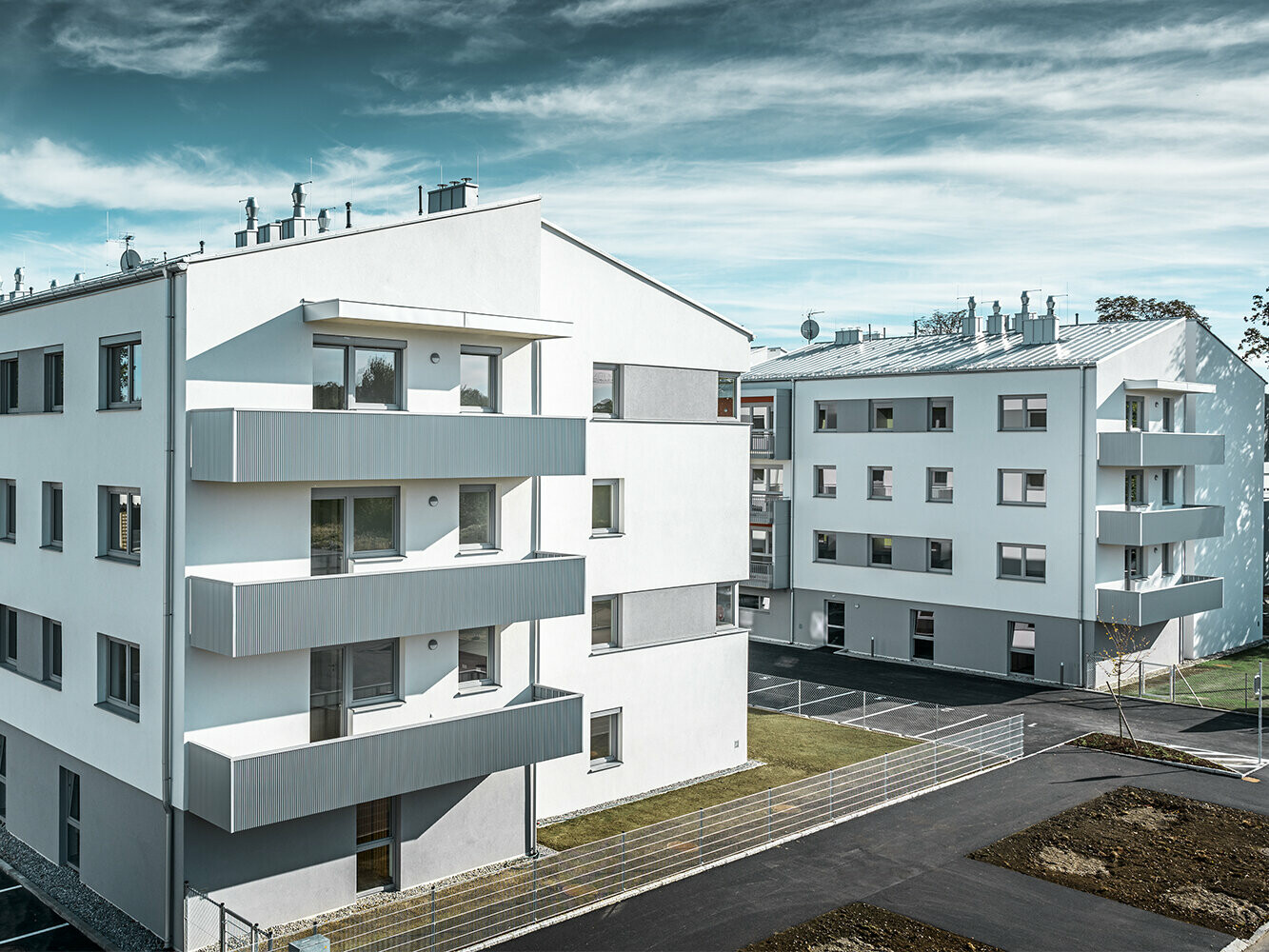 Modern lakókomplexum fehér homlokzattal és PREFA fogazott profilú erkéllyel, ezüstmetál színben