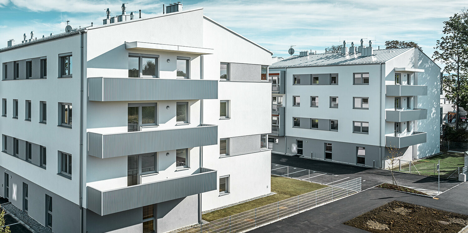 Modern lakókomplexum fehér homlokzattal és PREFA fogazott profilú erkéllyel, ezüstmetál színben