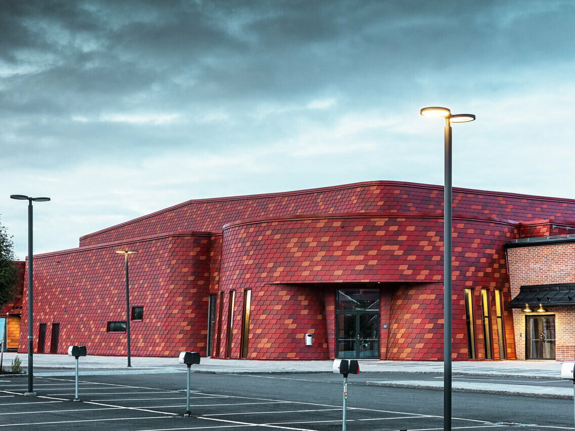 Aufnahme der Eis- und Eventhalle in Schweden. Für die Fassade wurde die PREFA Wandschindel in den Farben P.10 Oxydrot und zwei Sonderfarben Rotbraun und Braunrot verwendet.