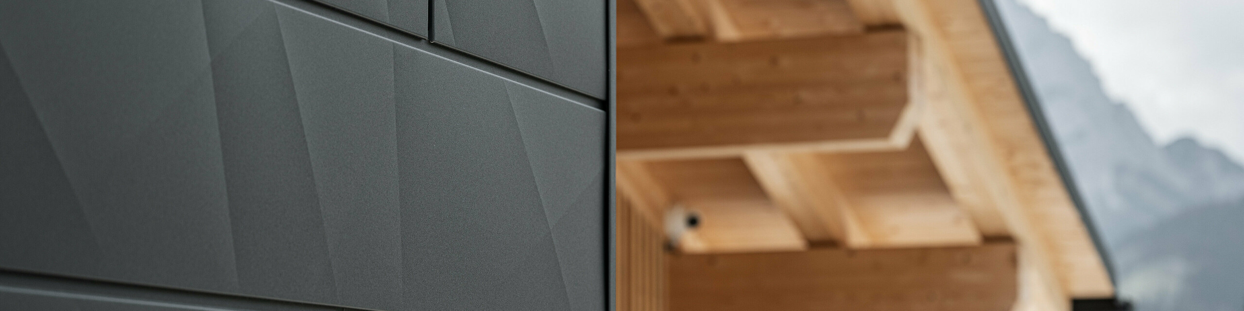 Közelkép a PREFA Siding.X homlokzatpanelekről P.10 fekete színben a Casa Hoffe épületén Sappada városában, Olaszországban. Az alumínium homlokzati rendszer modern, absztrakt kialakításban került alkalmazásra, amely vonzó kontrasztot képez a tetőszerkezet látható faelemeivel. Az innovatív homlokzati megoldás zökkenőmentesen illeszkedik az alpesi környezetbe, és a funkcionalitás, a tartósság és az esztétikus építészeti kultúra ötvözetét képviseli.