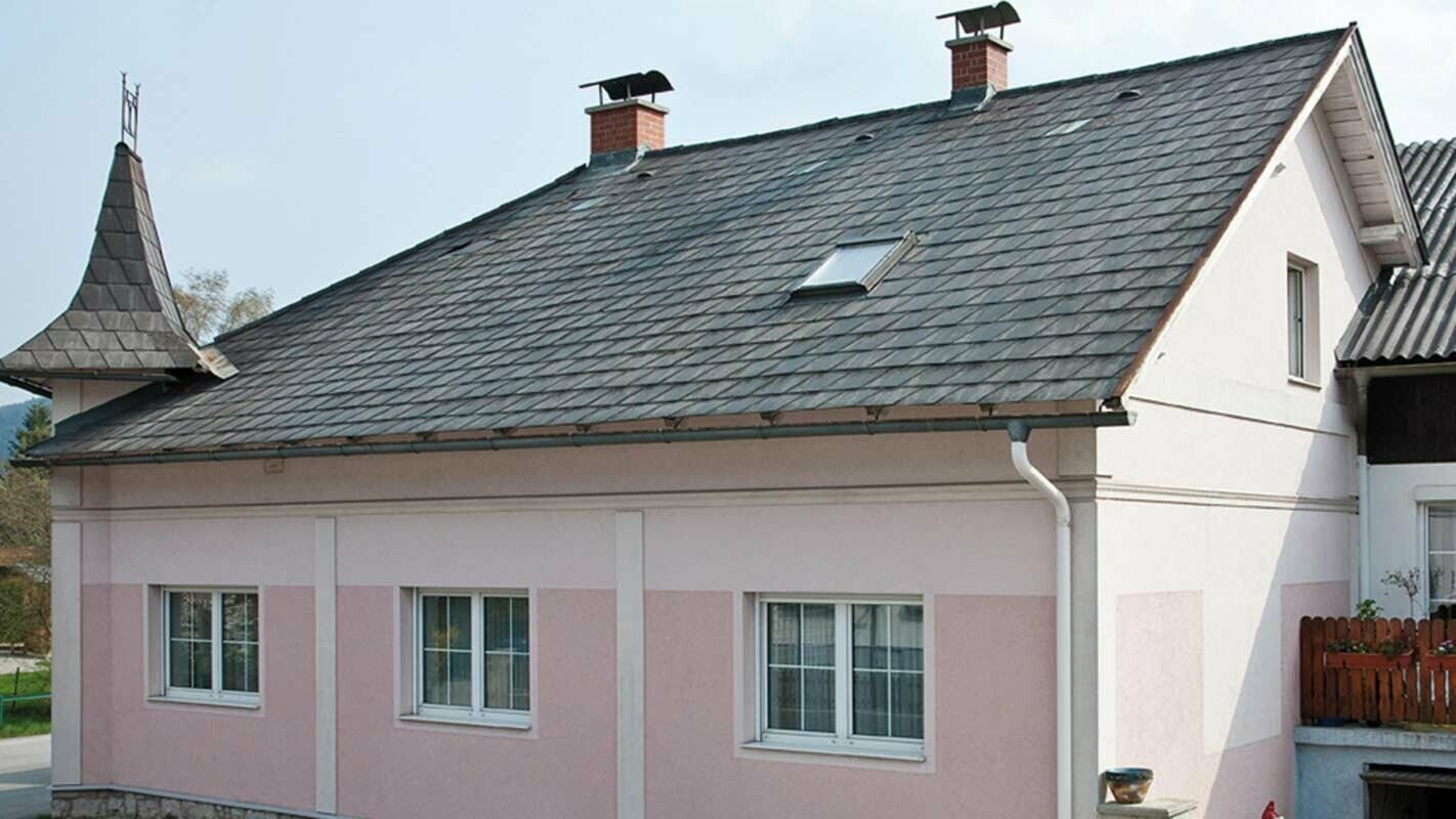 Társasház tetőfelújítás előtt, PREFA Classic elem, Ausztria – előtte eternit szálcement kisebb tornyok, rózsaszín homlokzat