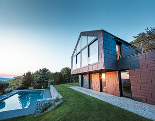 Családi ház alumíniumhomlokzata FX.12 P.10 antracit színű PREFA homlokzati panelekkel napnyugtakor. 