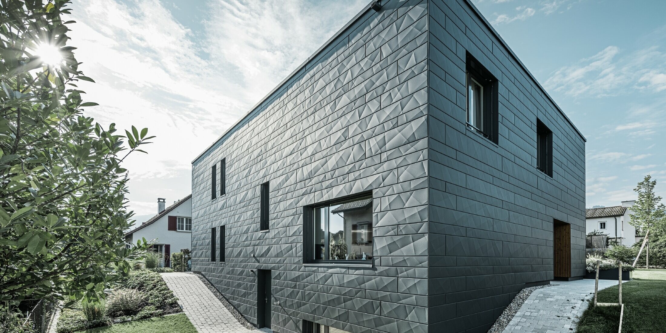 Seitenwinkelaufnahme des modernen Einfamilienhauses. Die Siding.X Fassade wirkt durch die Sonneneinstrahlung sehr dynamisch.