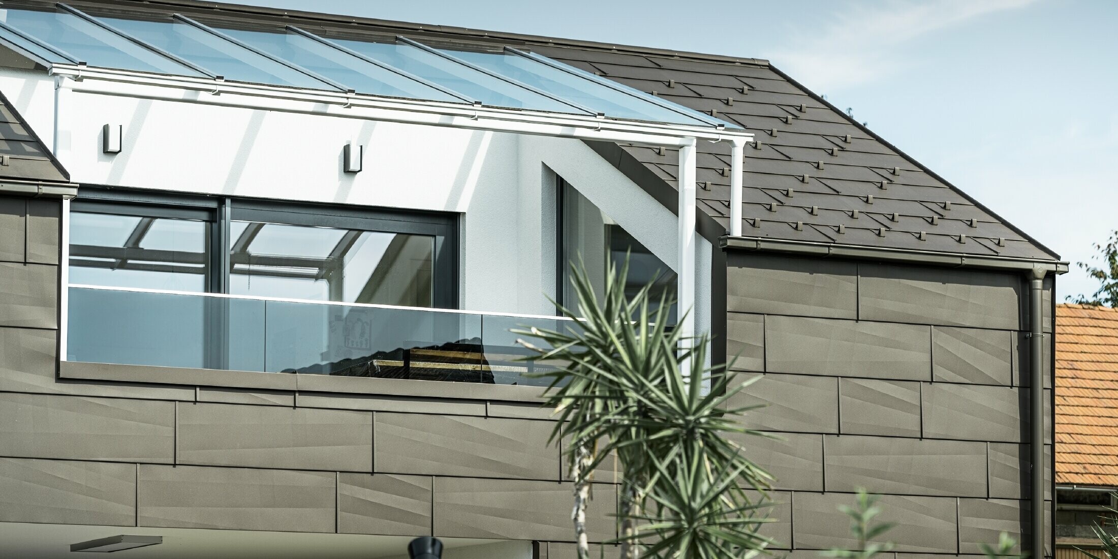 Bővítés PREFA komplett rendszerrel burkolt tetőterasszal, FX.12 PREFA tető- és homlokzatpanellel a tetőn és a homlokzaton. Ezenkívül a PREFA négyszögszelvényű ereszcsatorna PREFA lefolyócsővel és barna színű, gazdag tartozékokkal a tető-vízelvezetéshez.