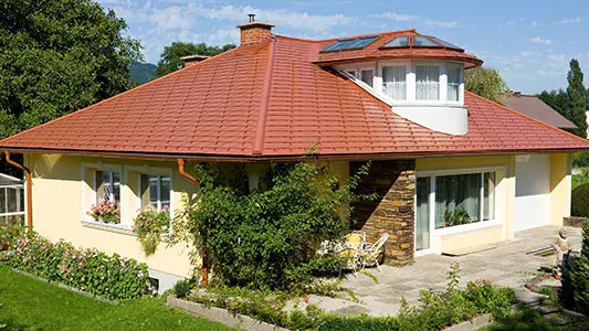 Einfamilienhaus mit Walmdach und Gaube, gedeckt mit PREFA Aluminiumschindeln in ziegelrot.
