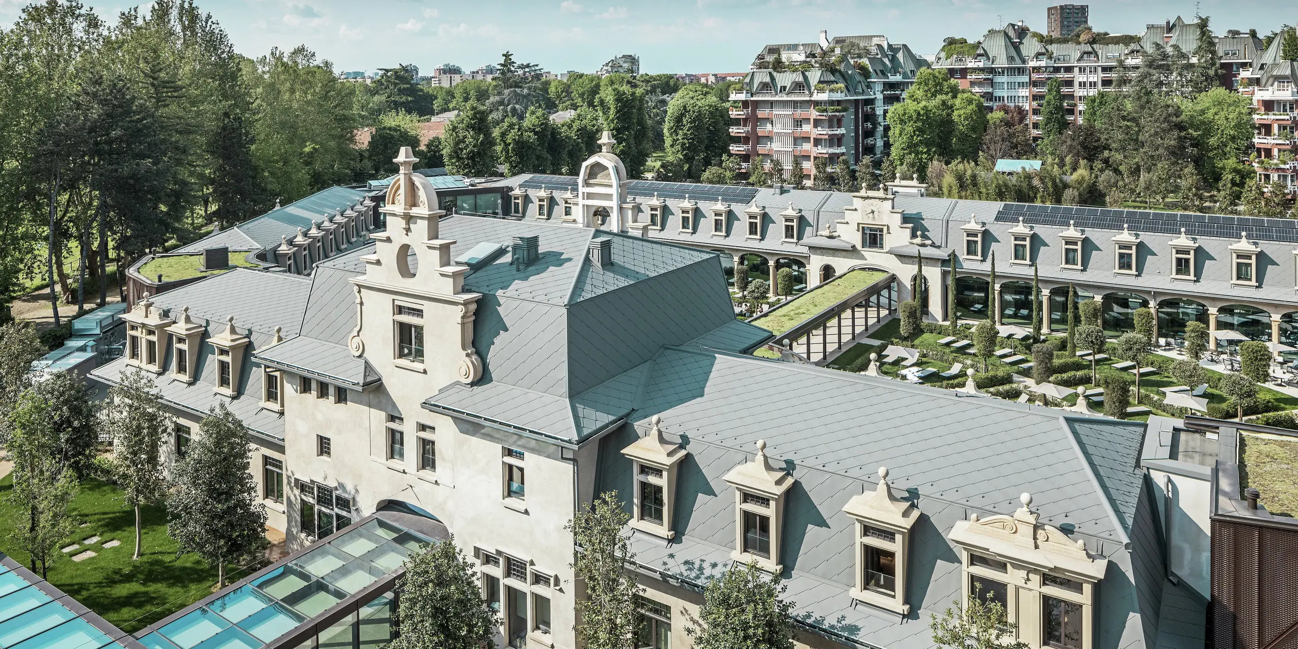 A „De Montel – Terme Milano” impozáns komplexumának teljes képe, műemléki védelem alatt álló szecessziós építészetével és modern wellness-környezetével. A nagy felületű tetőfedés PREFA 44 × 44-es tetőfedő rombusz, P.10 világosszürke színben elegáns egységességet kölcsönöz a komplexumnak. Az integrált fotovoltaikus modulok, a zöldtetők és az épületek közötti üvegkapcsolatok tükrözik a fenntarthatóság és a kortárs design iránti igényt városi környezetben.