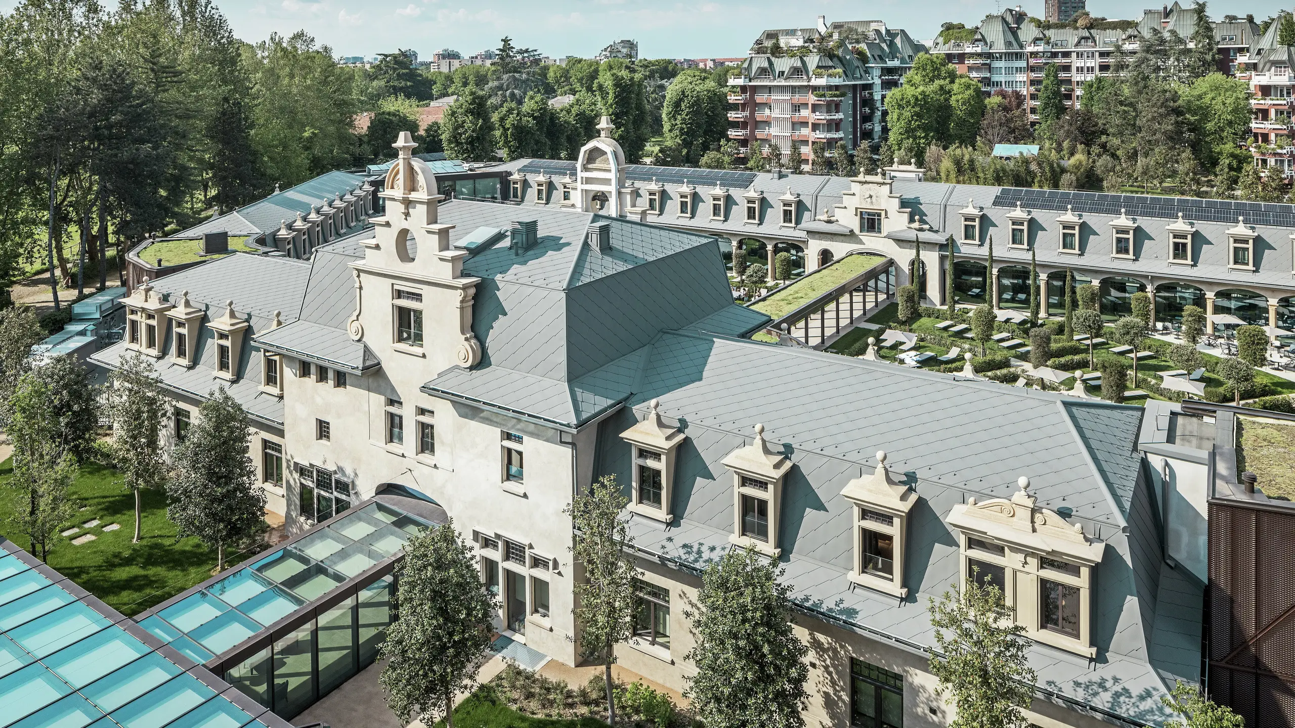 A „De Montel – Terme Milano” impozáns komplexumának teljes képe, műemléki védelem alatt álló szecessziós építészetével és modern wellness-környezetével. A nagy felületű tetőfedés PREFA 44 × 44-es tetőfedő rombusz, P.10 világosszürke színben elegáns egységességet kölcsönöz a komplexumnak. Az integrált fotovoltaikus modulok, a zöldtetők és az épületek közötti üvegkapcsolatok tükrözik a fenntarthatóság és a kortárs design iránti igényt városi környezetben.