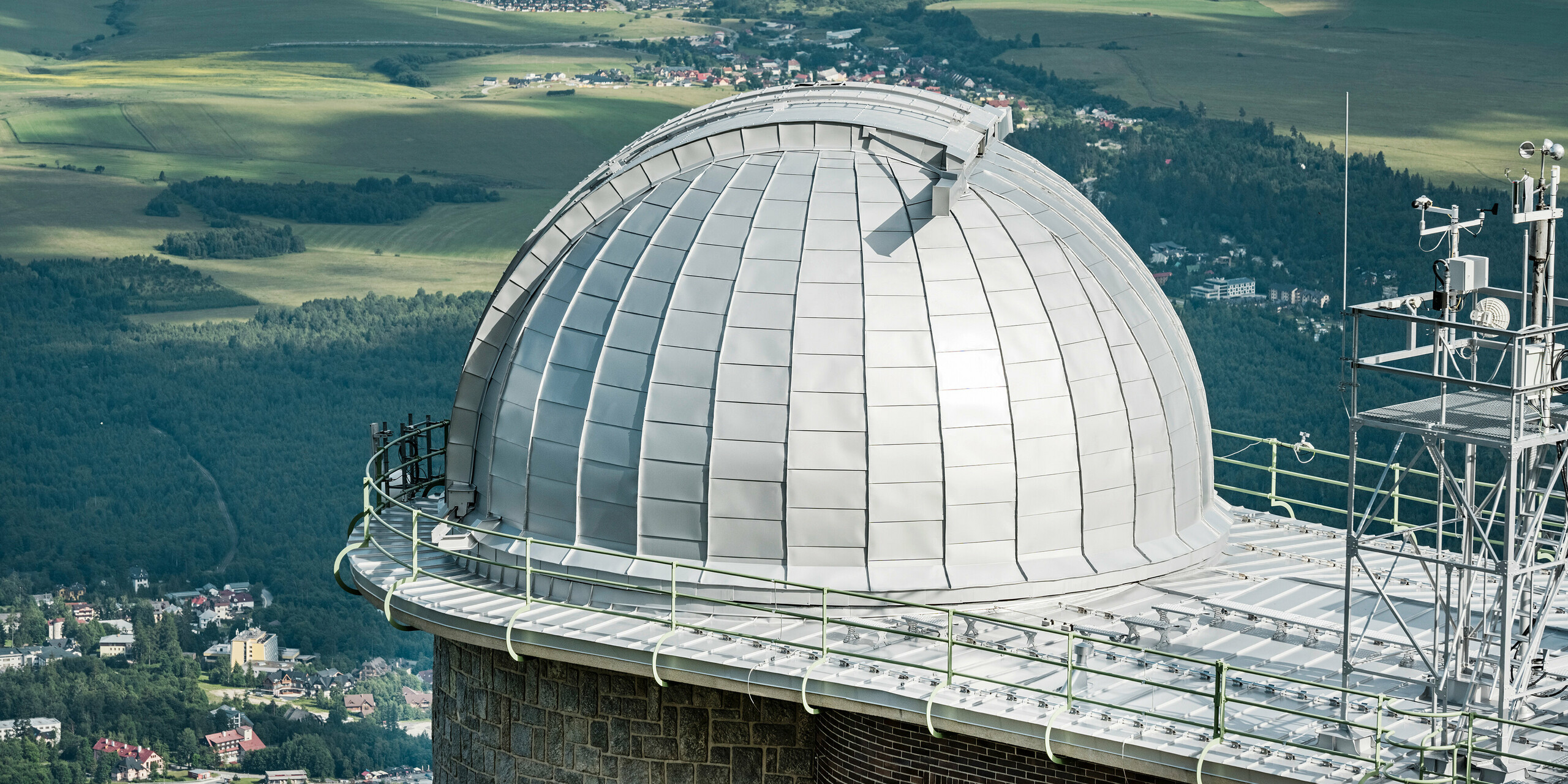Panoramablick auf die beeindruckende Kuppel des Observatoriums von Skalnate Pleso, das sich meisterhaft in die malerische Landschaft der Hohen Tatra einfügt. Die silbermetallische Aluminiumverkleidung PREFALZ schimmert im Kontrast zum üppigen Grün der umliegenden Wälder und den subtilen Konturen der ländlichen Landschaft. Dieses architektonische Juwel, das auf einer Höhe von 1.783 Metern über dem Meeresspiegel liegt, ist nicht nur ein Wahrzeichen astronomischer Entdeckungen seit 1943, sondern auch ein Beweis für die Langlebigkeit und Umweltverträglichkeit von PREFA Aluminiumprodukten, die durch eine 40-jährige Garantie abgesichert sind.