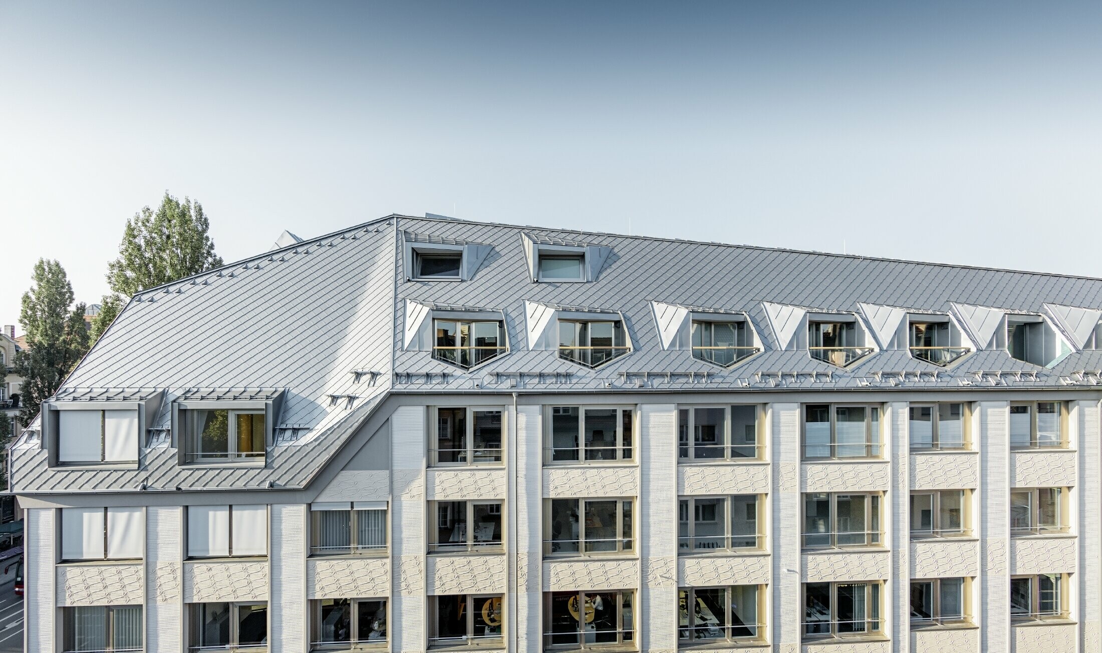 A müncheni Leopoldstraße és a Hohenzollernstraße sarkán álló lakó- és üzletház felújított manzárd lakásai nagyvonalú, galériázott tereket kínálnak a PREFA tetőfedő rombusz fedés alatt.