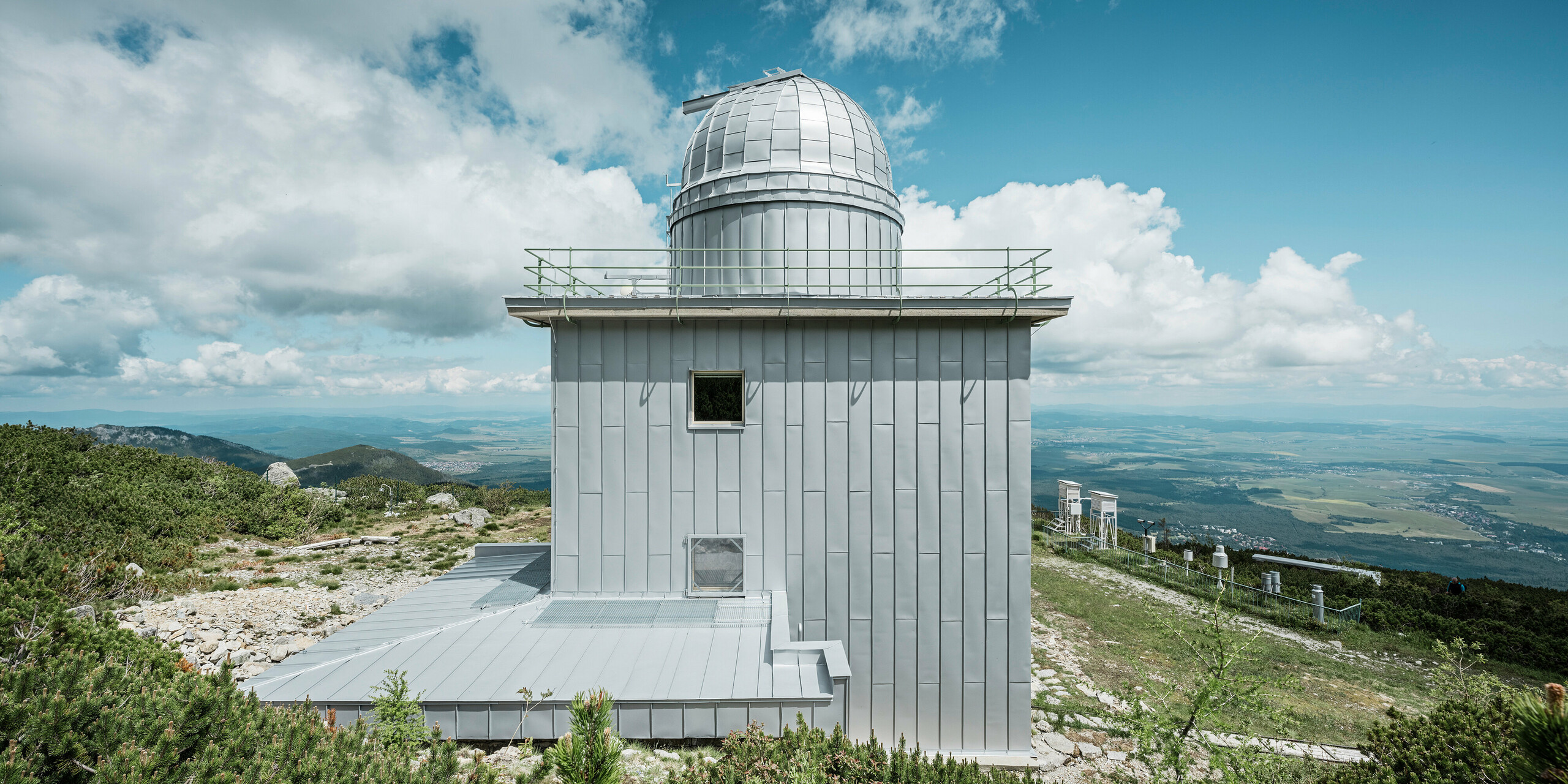 Modernisierter hinterer Teil des Observatoriums Skalnaté Pleso in der Natur der Hohen Tatra, mit einer Dach- und Fassadenverkleidung aus PREFALZ in Silbermetallic. Die klaren Linien und die metallische Eleganz des Materials ergänzen die raue Schönheit der slowakischen Berglandschaft, während die Konstruktion selbst den extremen Witterungsbedingungen der exponierten Lage in den Bergen standhält. Dank des robusten Aluminiums ist die Sternwarte langlebig und fügt sich ästhetisch in die beeindruckende Umgebung ein.