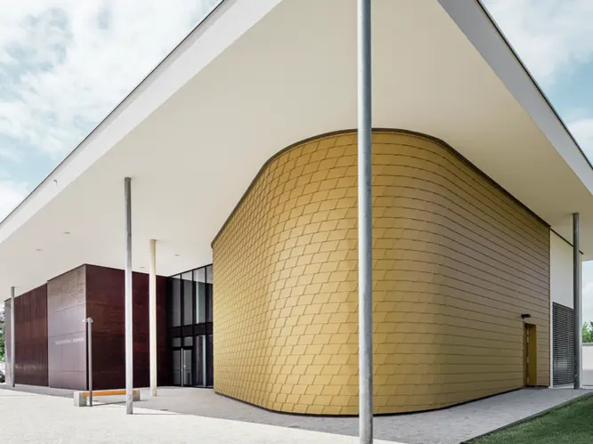 Seitliche Aufnahme der Landesmusikschule in Buchkirchen. Die Fassade wurde mit PREFA Wandschindeln in der Sonderfarbe Mayagold verkleidet.