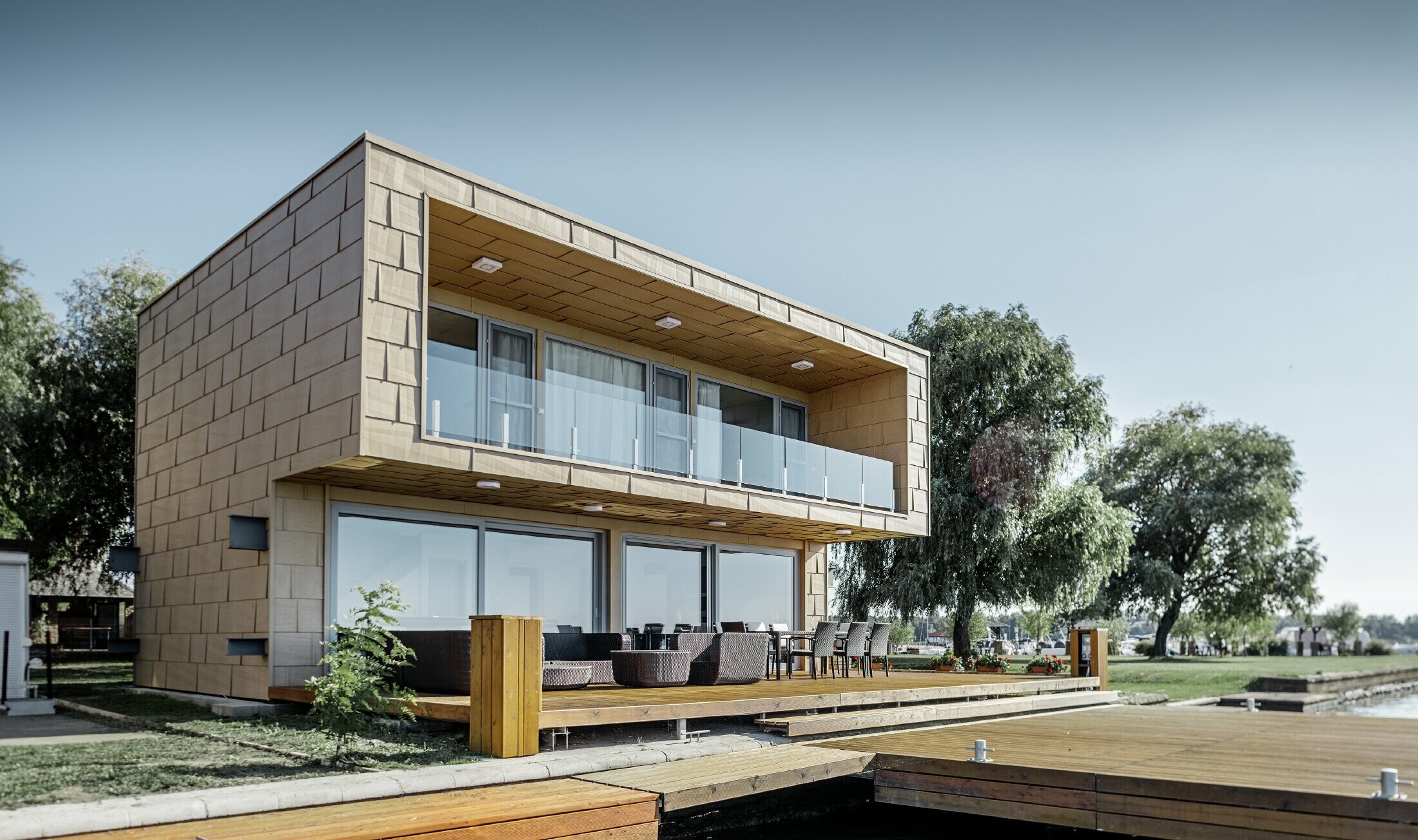 Új építésű lapostetős hétvégi ház a vízparton, hatalmas üveg felülettel és homokszínű tört vonalú alumínium homlokzatburkolattal