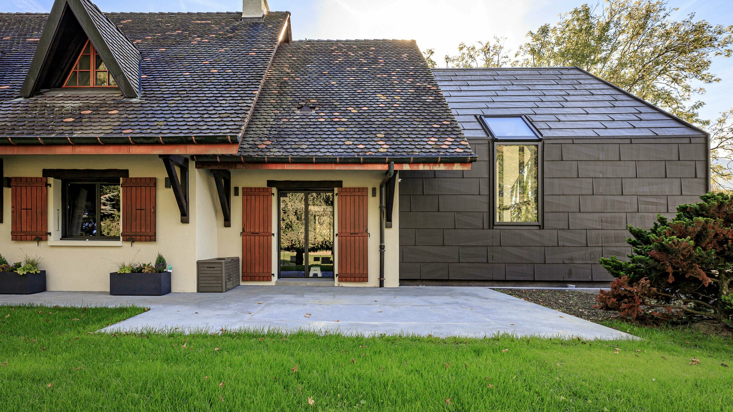 PREFA FX.12 tető- és homlokzatburkoló panelek P.10 barna színben, kontrasztos díszítőelemként egy családi ház bővítményén Lullyban