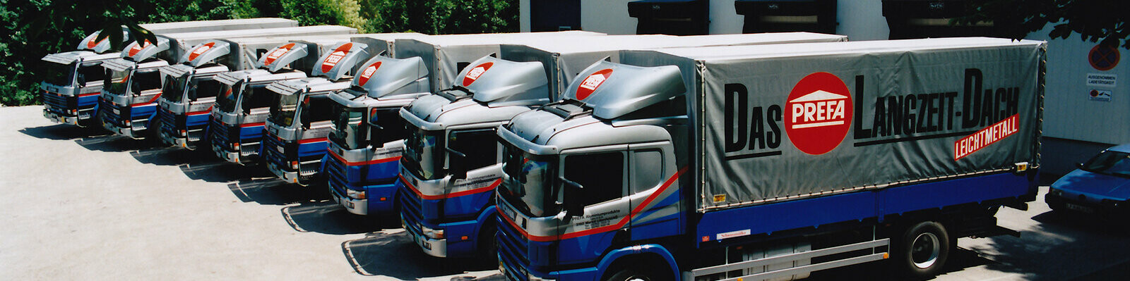 Acht ehemalige PREFA LKWs in Blau und Silber mit PREFA Logo stehen in einer Reihe 