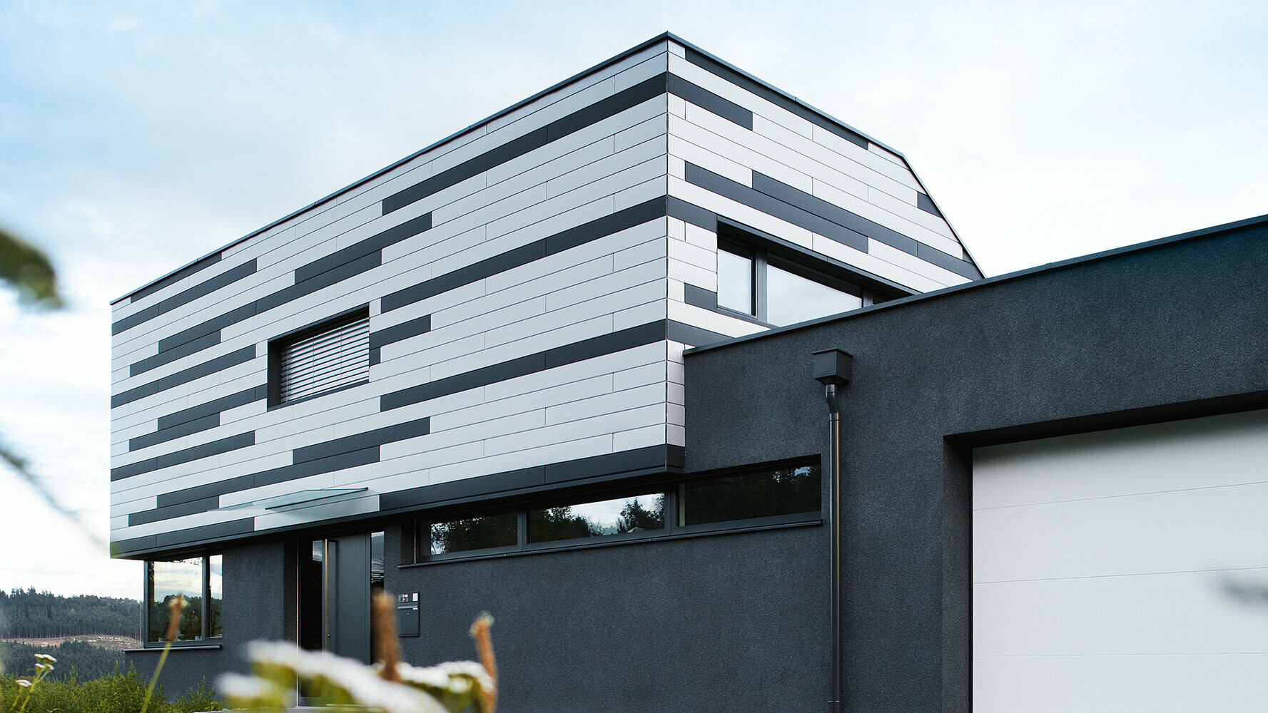Modern családi ház kreatív homlokzati kialakítással; A PREFA Siding elemek ezüst és matt antracit kombinációban díszítik a homlokzatot.