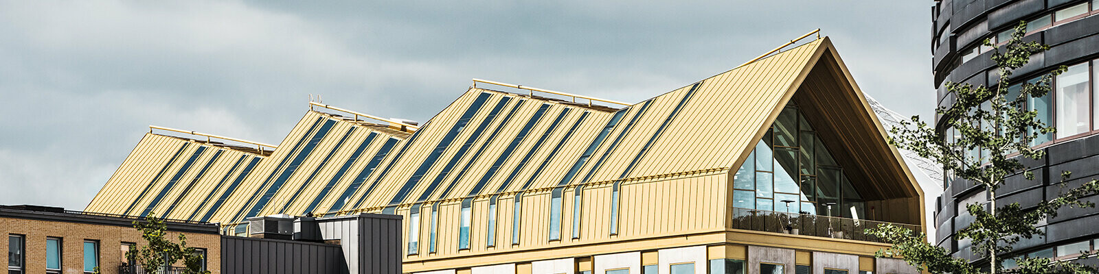 seitliche Frontansicht des Gebäudes in Malmö eingedeckt mit dem Dachsystem PREFALZ in der Sonderfarbe Jaisalmer Gold
