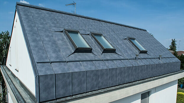 Nyeregtetős tetőtér építése tetőtéri ablakokkal. A tető közvetlenül átnyúlik a homlokzaton és márványszürke állókorcos Prefalz fedi.