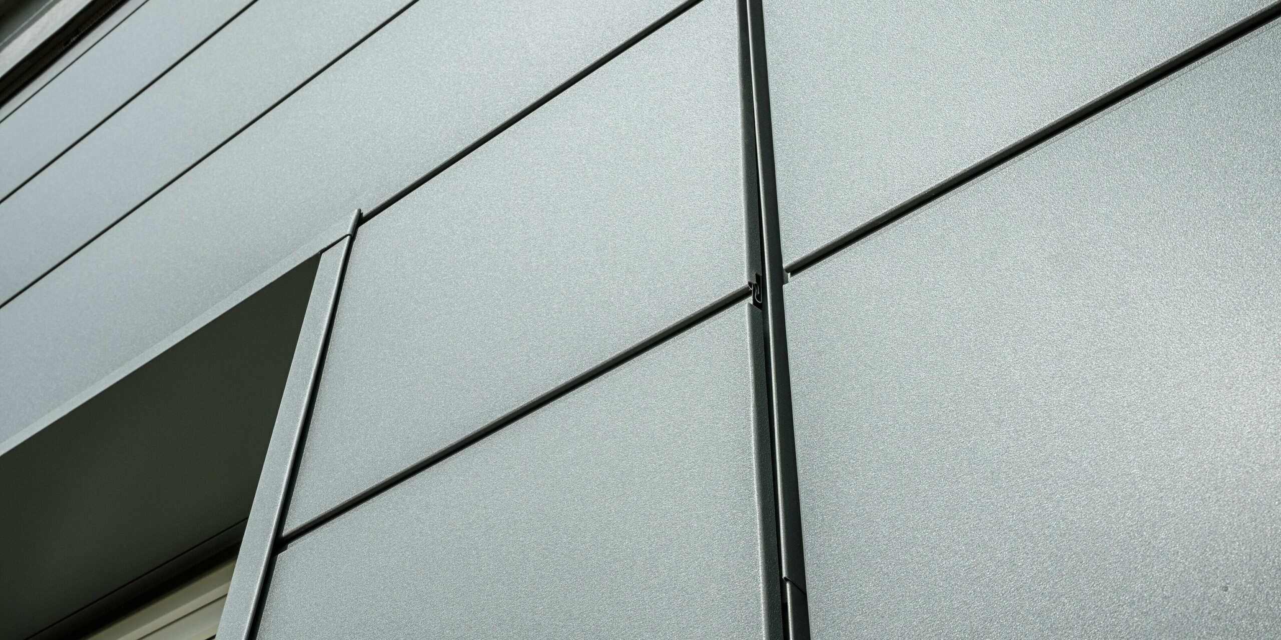 Die Fassade der Kaminkehrerinnung in Bindlach zeigt moderne PREFA Sidings in P.10 Dunkelgrau. Die klar strukturierten Aluminium-Paneele sind nicht nur ein optisches Highlight, sondern auch äußerst widerstandsfähig gegenüber Witterungseinflüssen. In der Detailaufnahme sind die präzise verlegten Blech-Paneele und die stilvolle, schlichte Linienführung deutlich zu erkennen.