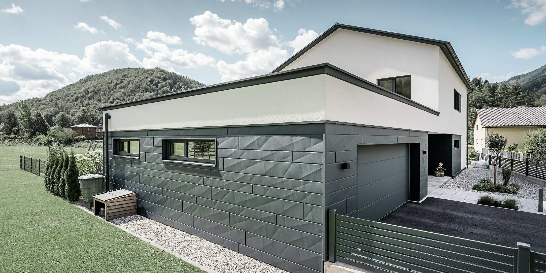 Modernes Einfamilienhaus und Garage mit einer Siding.X Fassade in P.10 Anthrazit. Es befindet sich in einer ländlichen Umgebung.