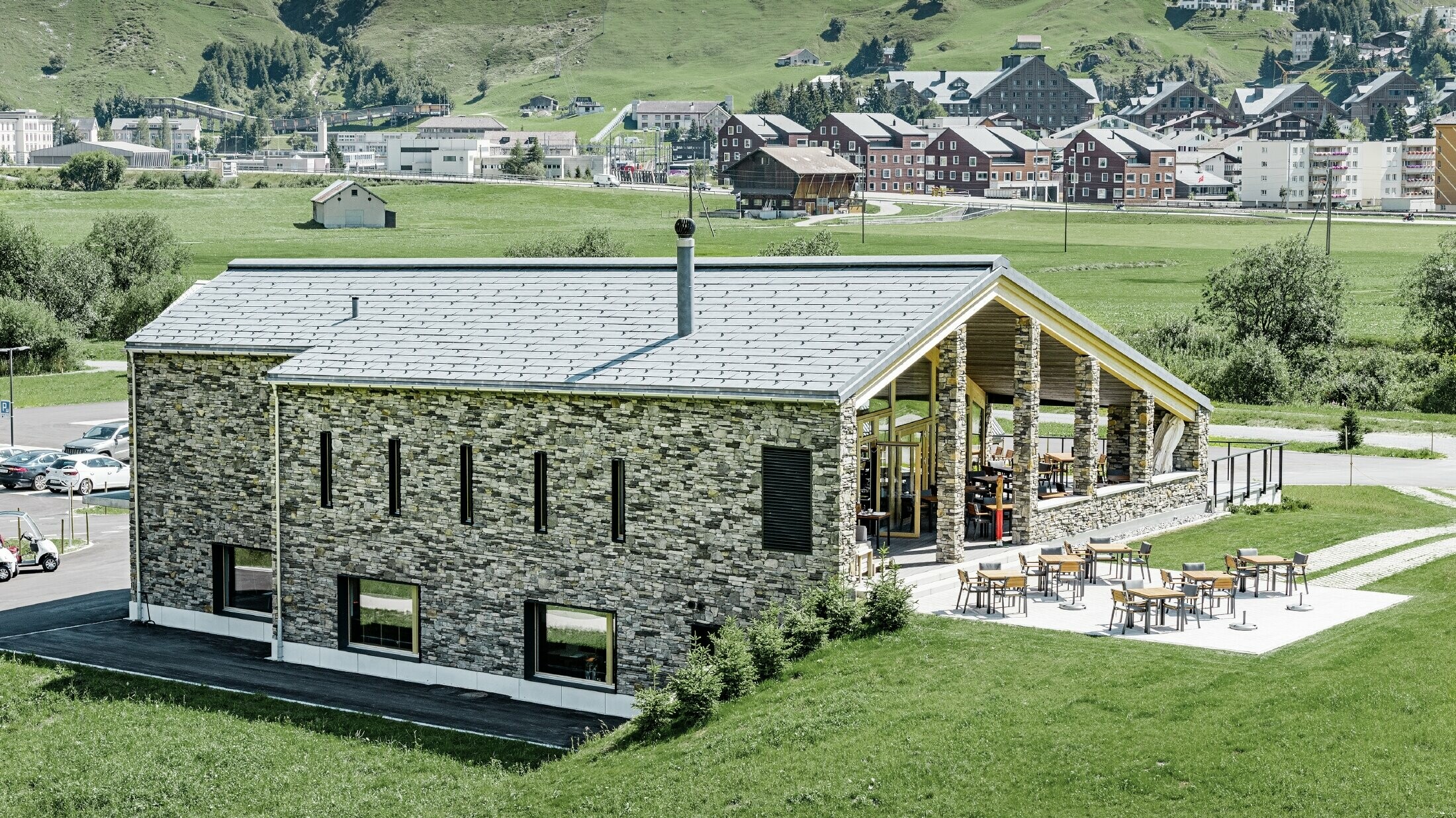 Az andermatti golfpálya modern épülete kőburkolattal és márványszürke PREFA FX.12 alumínium tetőfedő panel fedéssel