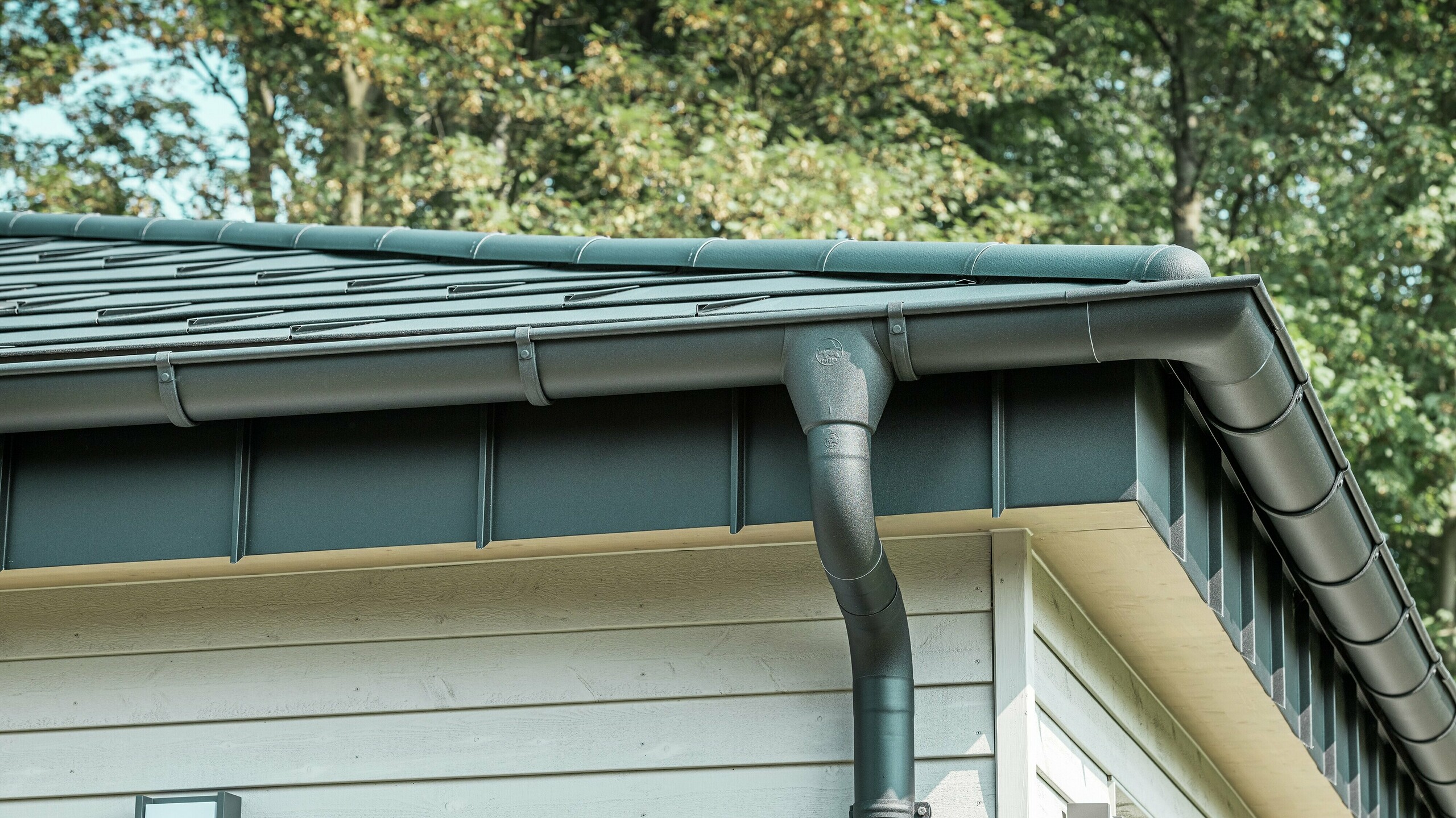 Detailansicht der PREFA Dachentwässerung eines Bungalows in Rommerskirchen. Die hochwertige Saumrinne und das Ablaufrohr in P.10 Schwarz bieten eine sichere Dachentwässerung bei Regen. Die langlebigen PREFA Aluminiumprodukte verbinden Funktionalität mit modernem, elegantem Design.