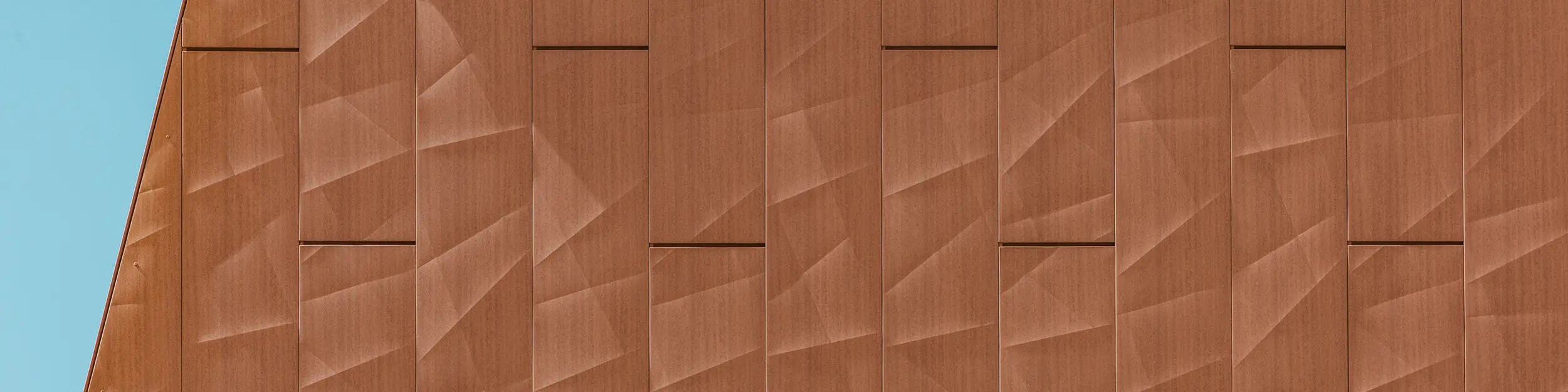Detailaufnahme der PREFA Siding.X Aluminiumfassade am Trinkwasserpumpwerk WML in Lottum mit präzise gefalteten Paneelen in warmer Rostoptik als visueller Eyecatcher. Die geometrisch strukturierte Oberfläche erzeugt ein faszinierendes Spiel aus Licht, Schatten und feinen Linien, das je nach Blickwinkel lebendig changiert. Die hochwertigen PREFA Aluminium-Paneele überzeugen durch geringes Gewicht, hohe Witterungsbeständigkeit, Farbkonstanz und vollständige Recyclingfähigkeit – für eine langlebige, nachhaltige und wartungsarme Fassadenlösung.