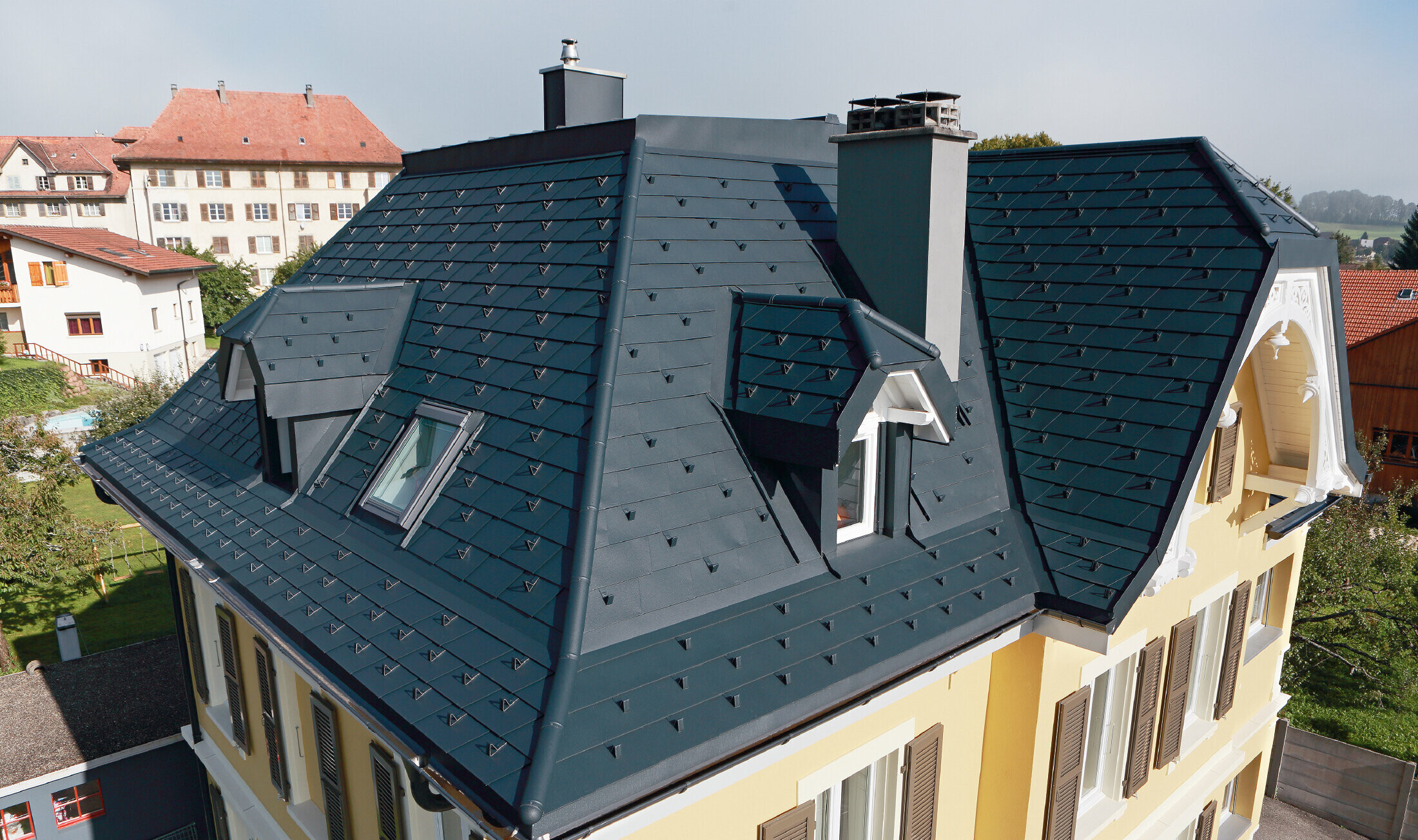 Svájci villa, a tetőn számtalan vápa és kisebb álló tetőablak található, a tetőt P.10 antracit színű PREFA alumínium zsindellyel fedték