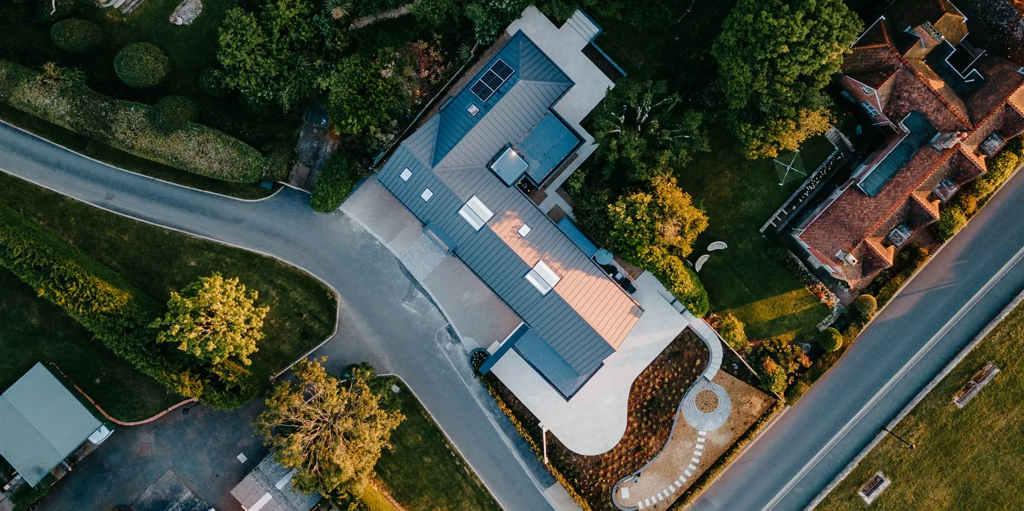 Vogelperspektive auf ein neu gestaltetes Wohnhaus auf der Isle of Wight, dessen Dach mit dunkelgrauem PREFALZ Aluminium verkleidet ist. Die klare, rechteckige Form des Daches steht im Kontrast zur umliegenden, traditionellen Architektur und den grünen Gartenanlagen. Dieses Bild zeigt, wie das Haus mit seiner modernen Gestaltung und PREFALZ Bedachung eine Brücke zwischen zeitgenössischem Wohnkomfort und der klassischen englischen Landschaft schlägt.