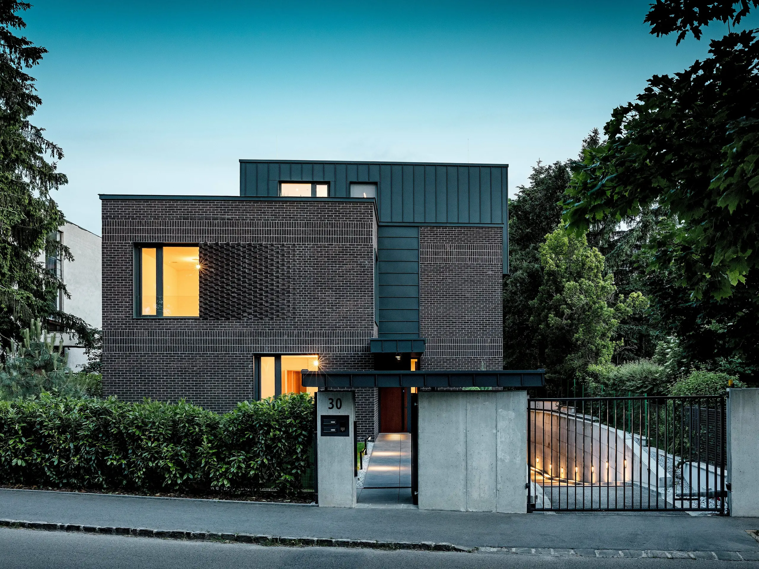 Das Bild zeigt ein modernes Wohnhaus in Budapest, dessen kubisches Dach aus PREFALZ-Aluminium in der Farbe P.10 Anthrazit einen markanten Kontrast zur historischen Umgebung bildet. Die vertikalen, stehenden Falze erzeugen ein interessantes Lichtspiel und unterstreichen die klare architektonische Formensprache. Die hochwertigen Aluminiumprodukte von PREFA verleihen dem Gebäude nicht nur ein elegantes, zeitloses Erscheinungsbild, sondern zeichnen sich auch durch ihre Langlebigkeit, Witterungsbeständigkeit und präzise Verarbeitung aus. Der anthrazitfarbene Teil der Fassade und des Daches setzt einen starken optischen Akzent und betont den innovativen Charakter des Gebäudes.