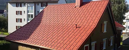 Alumínium PREFA tetőlemezzel fedett nyeregtető. Téglavörös tető hófogókkal és kéménnyel